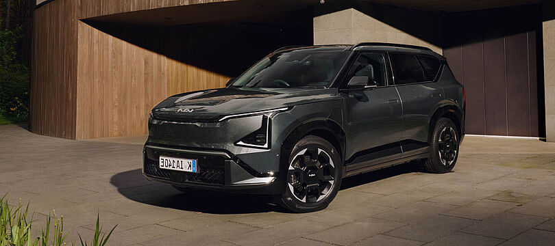 Kia EV5 in Grau vor Haus aus Holz